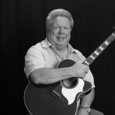 Posed black and white photograph of musician Dave more sitting on a stool